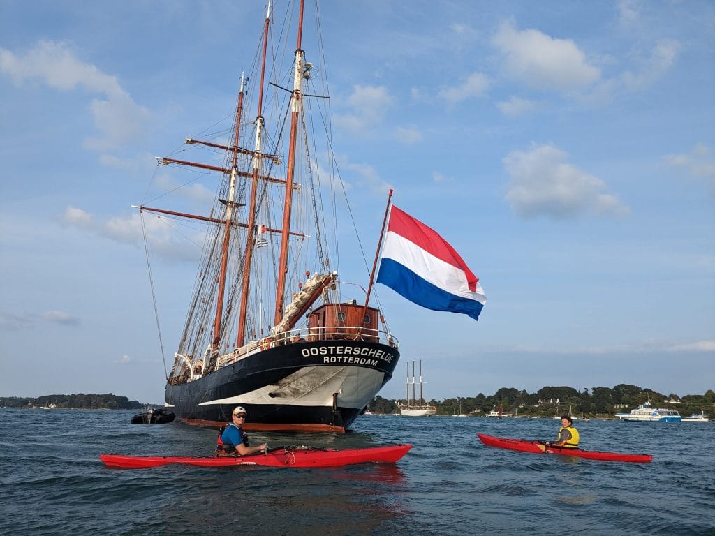 Single kayaks paddling around traditional sailing ships during Gulf of Morbihan Week.