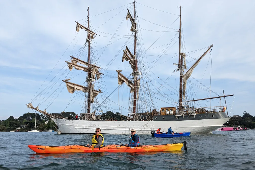 Kayak biplace sur l'eau devant un voilier de la semaine du Golfe du Morbihan.